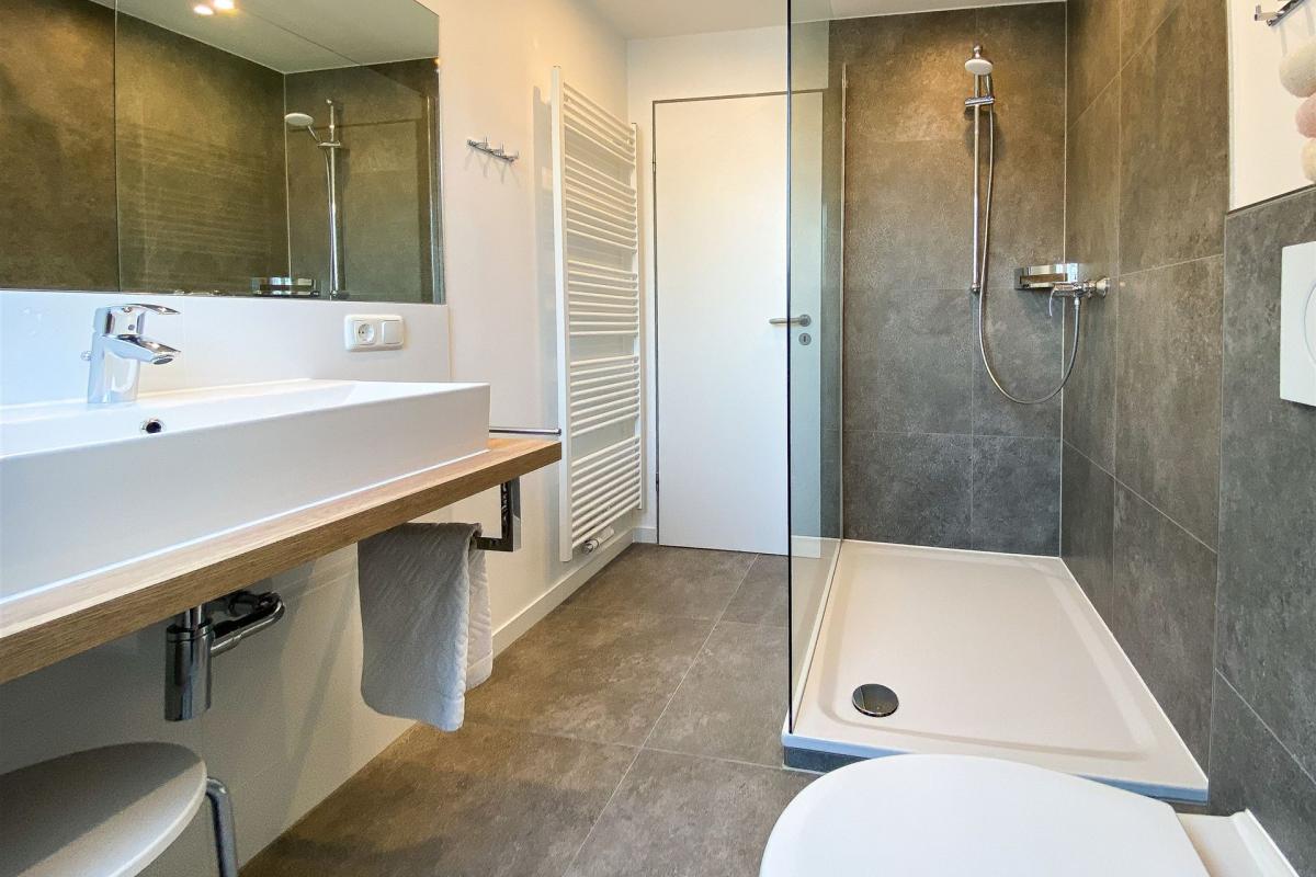 Moderne Waschtischkonsole und großzügige Dusche im hellen Bad des Apartments W4