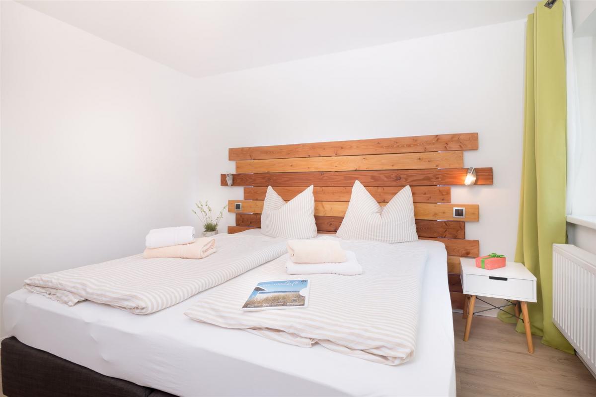 Schlafzimmer mit Doppel-Boxspringbett und moderner Holz-Rückwand im Strandhaus-Apartment K1